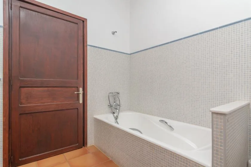 A tiled bathroom with a bathtub beside a wooden door.