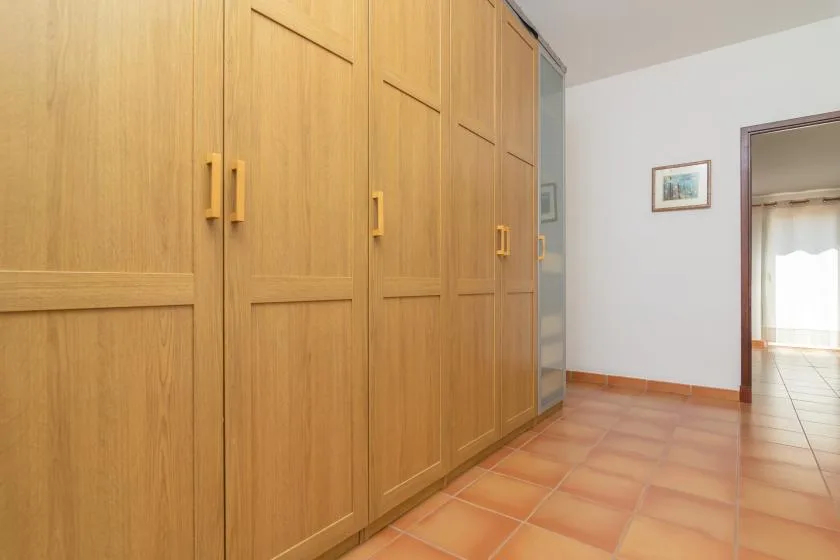 A room with tall wooden cabinets, terracotta-colored floor tiles, and a doorway.