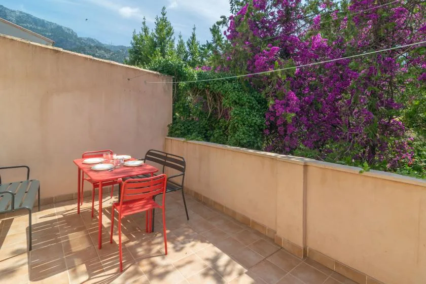 A tiled outdoor terrace with red seating and a table beneath flowering trees.