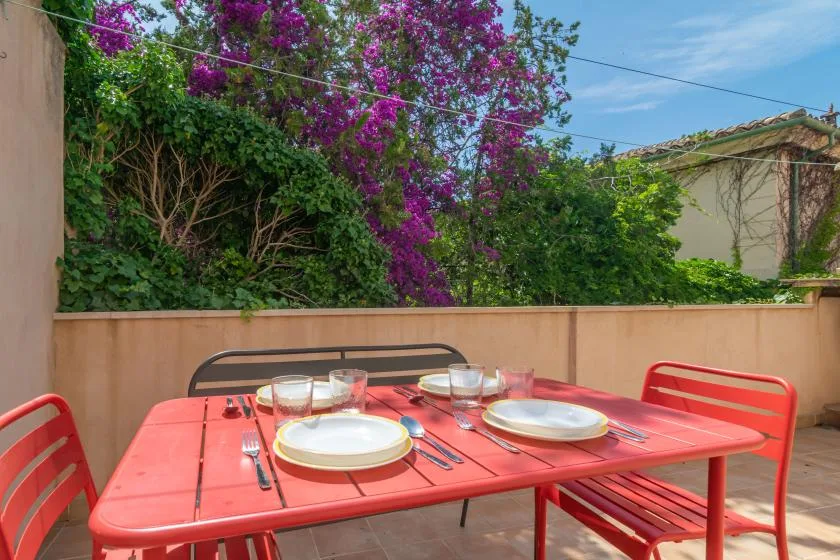 An outdoor dining area with a red table set with plates and glasses.