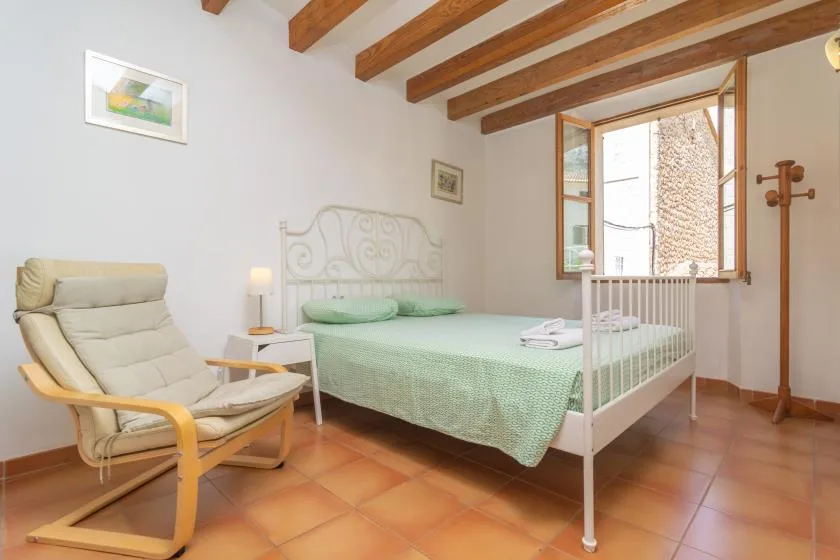 A bedroom with a bed, a cushioned chair, and an open window.