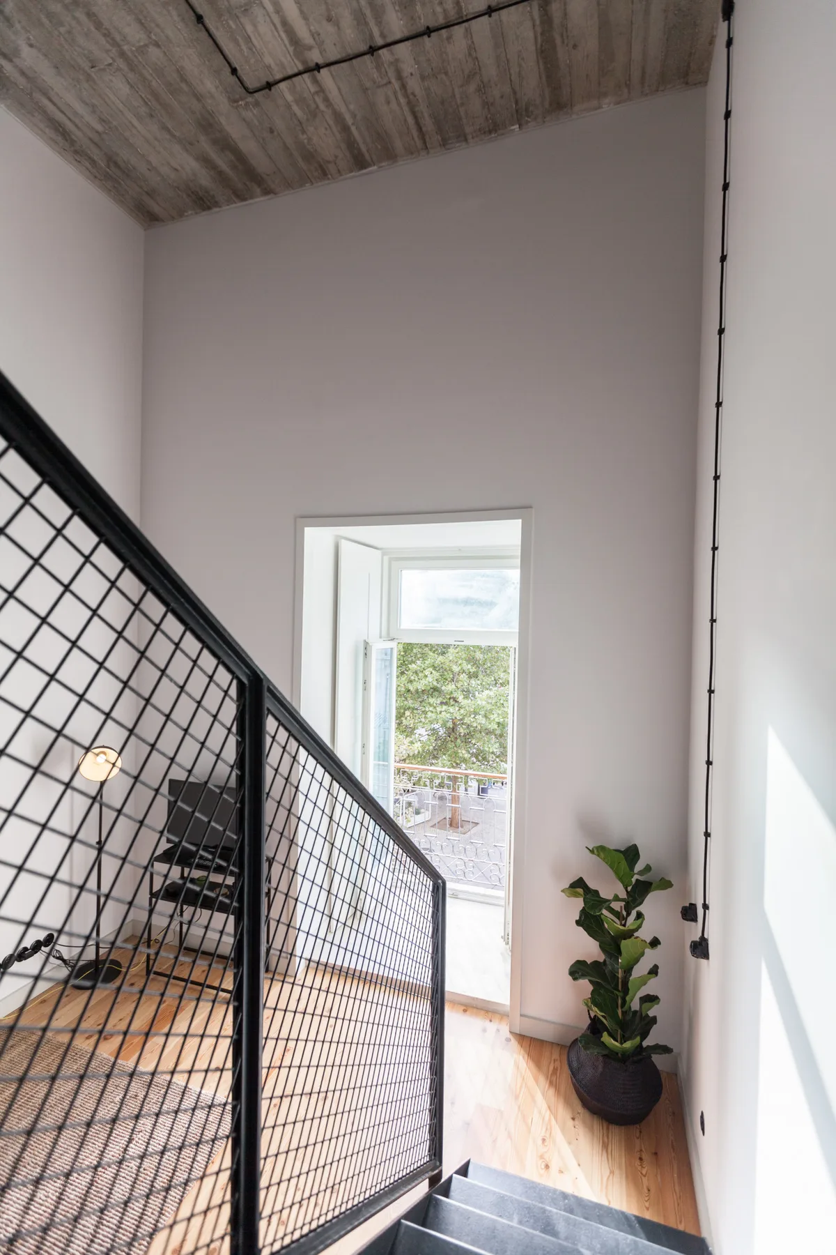 A tall interior landing with a black metal railing, stairs, and a doorway.