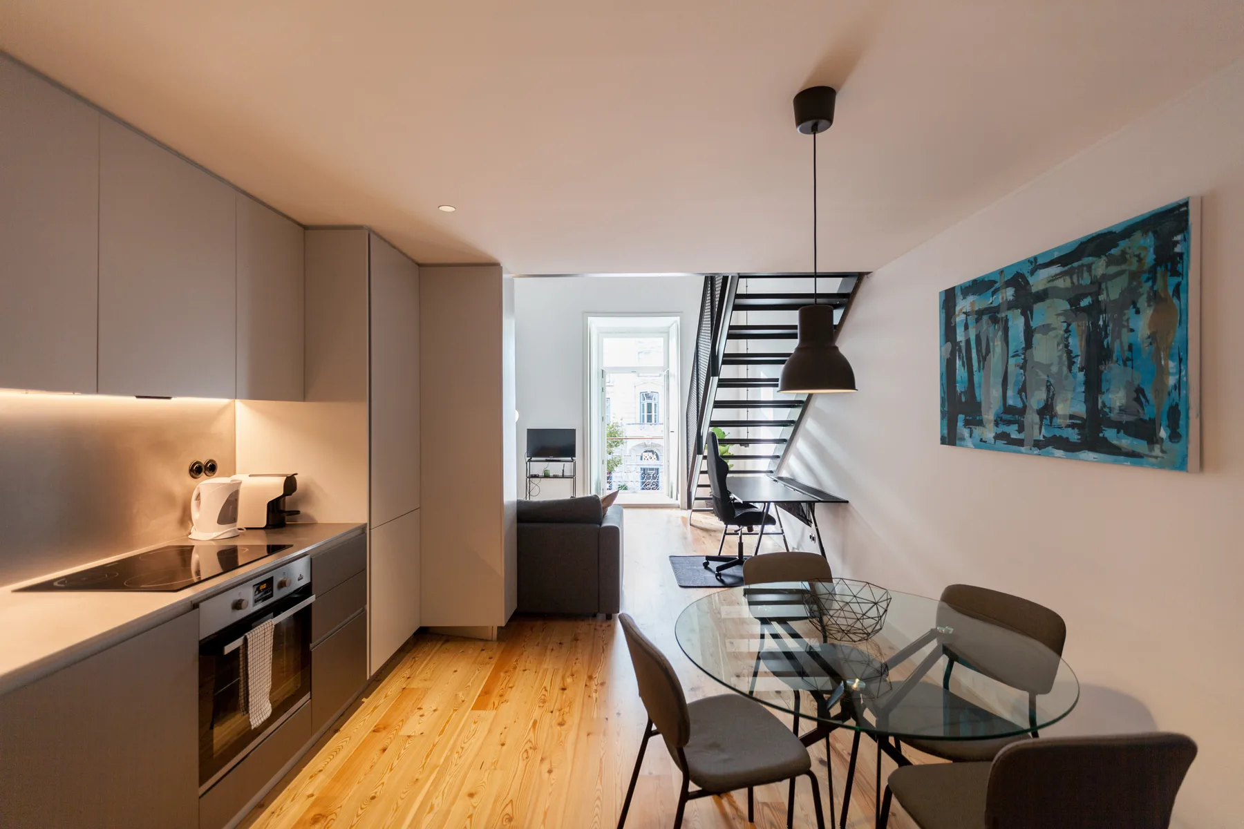 A modern apartment interior with a kitchen, dining table, and staircase.