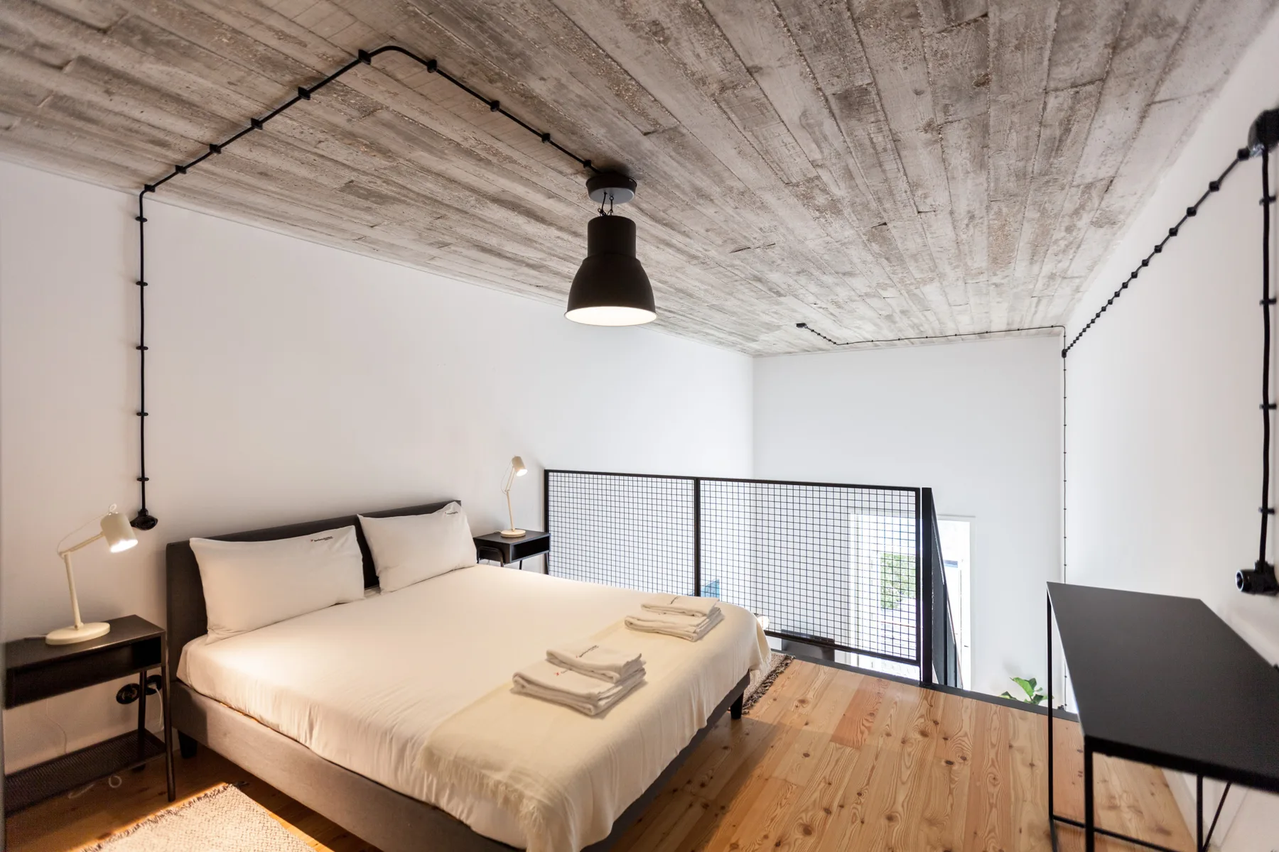 A bedroom with a double bed, bedside tables, and a black mesh railing.
