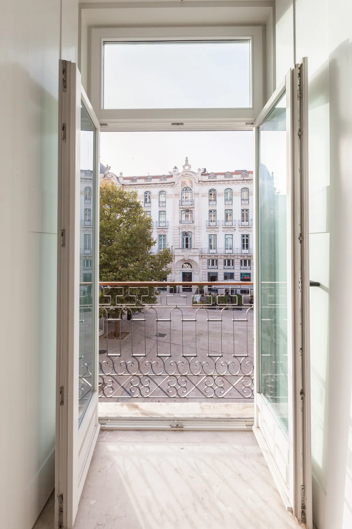 An open window looks out onto a balcony and a neighboring building.