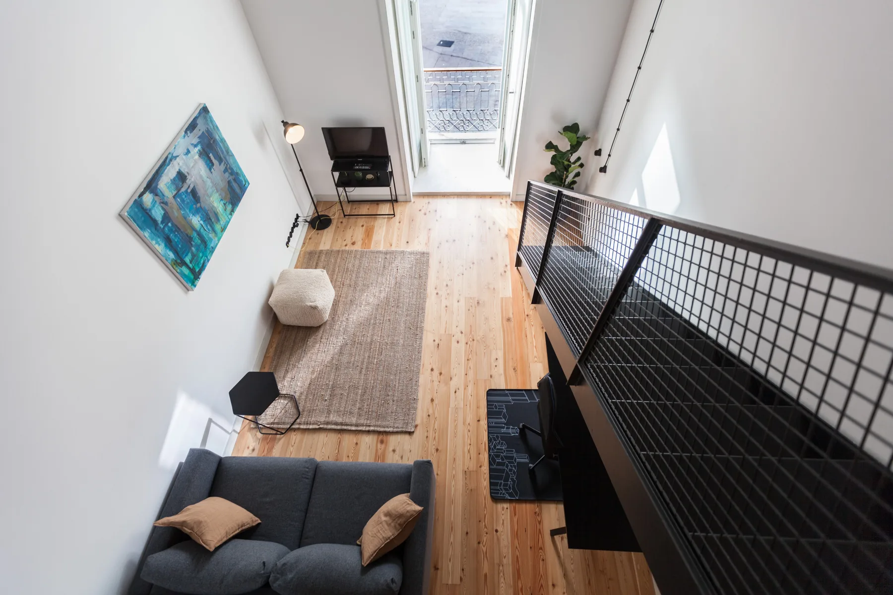 A bright living room with a sofa, rug, and black metal mezzanine railing.