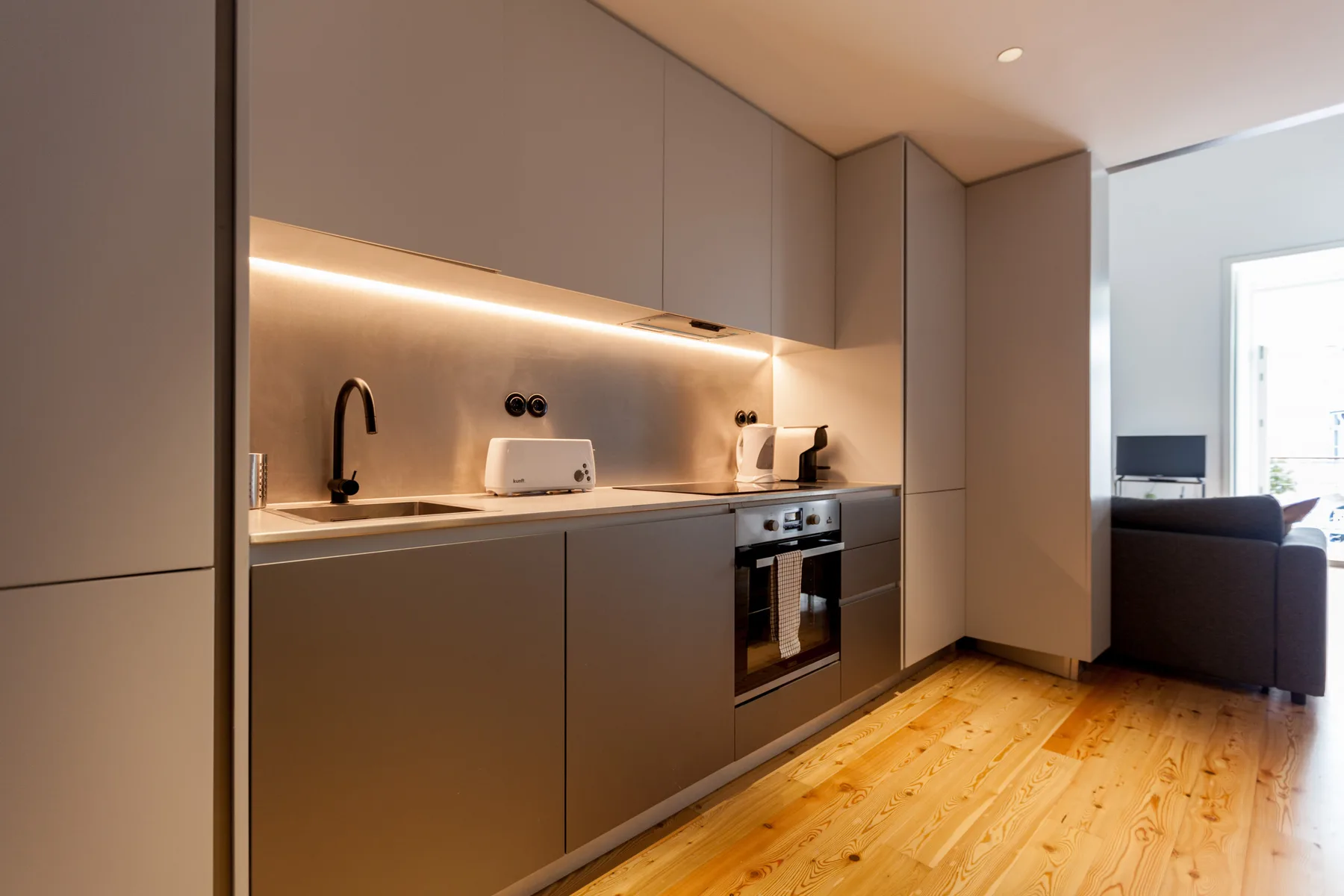 A modern kitchen opens into a living area with a television and seating.