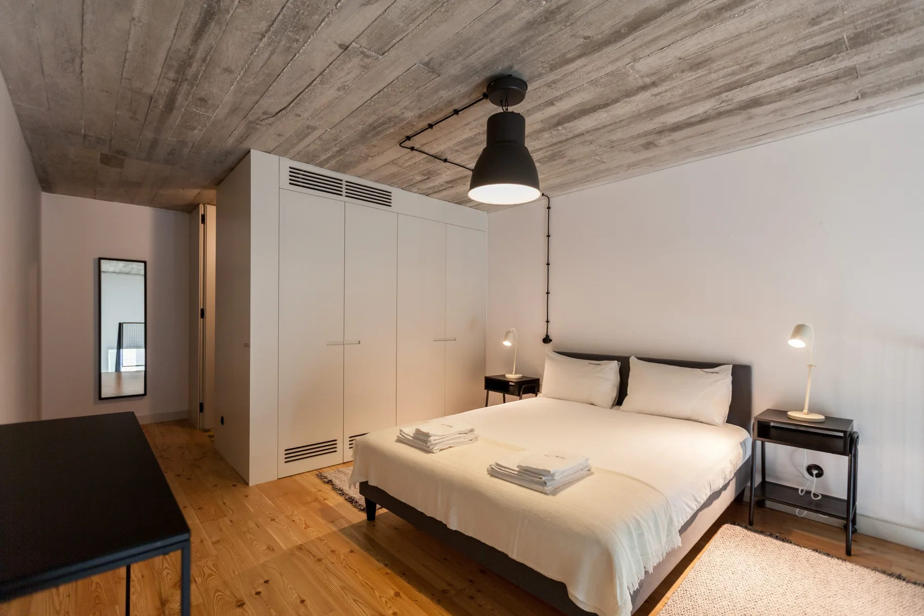A bedroom with a large bed, white wardrobes, and a wood floor.