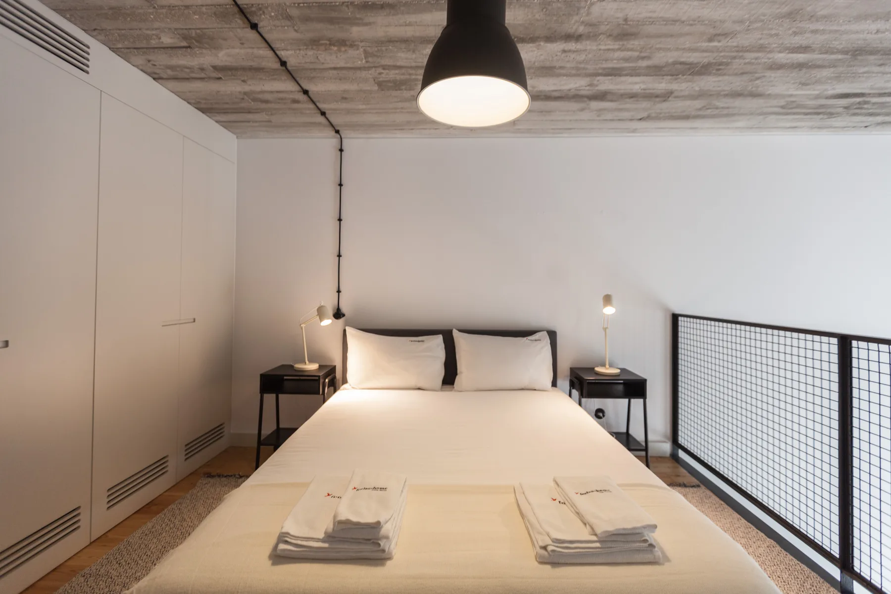 A bedroom with a neatly made bed beside a mesh railing.