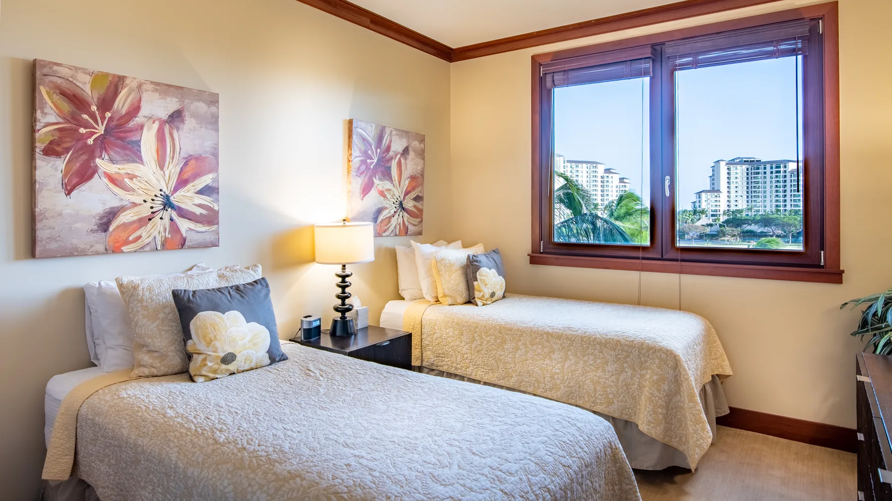 Un dormitorio con dos camas, cuadros florales y una ventana amplia.