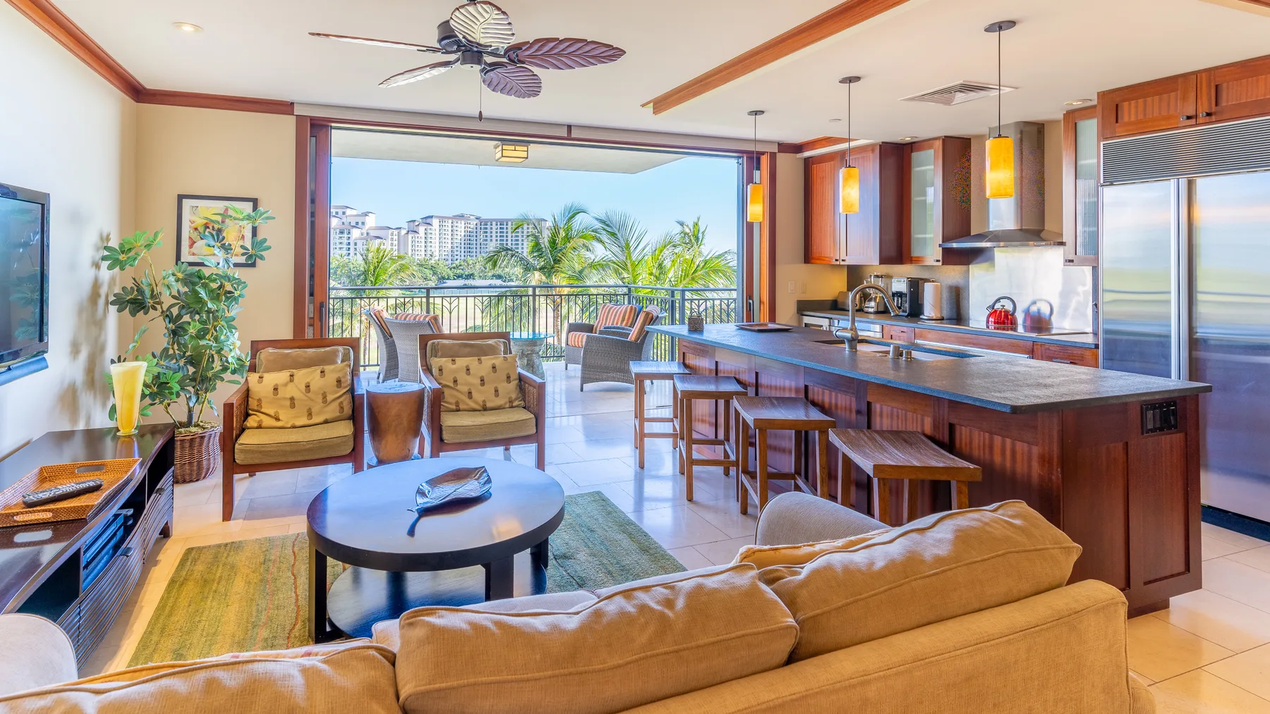 Una sala de estar se abre a un balcón junto a una isla de cocina y taburetes.