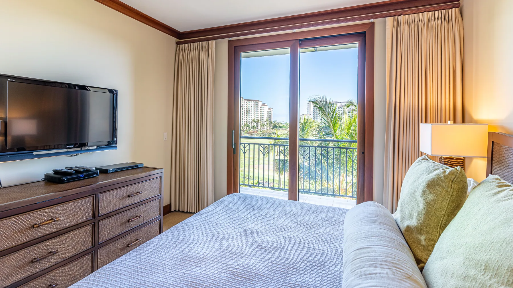 Un dormitorio con cama, televisor y puertas de vidrio que dan a un balcón.
