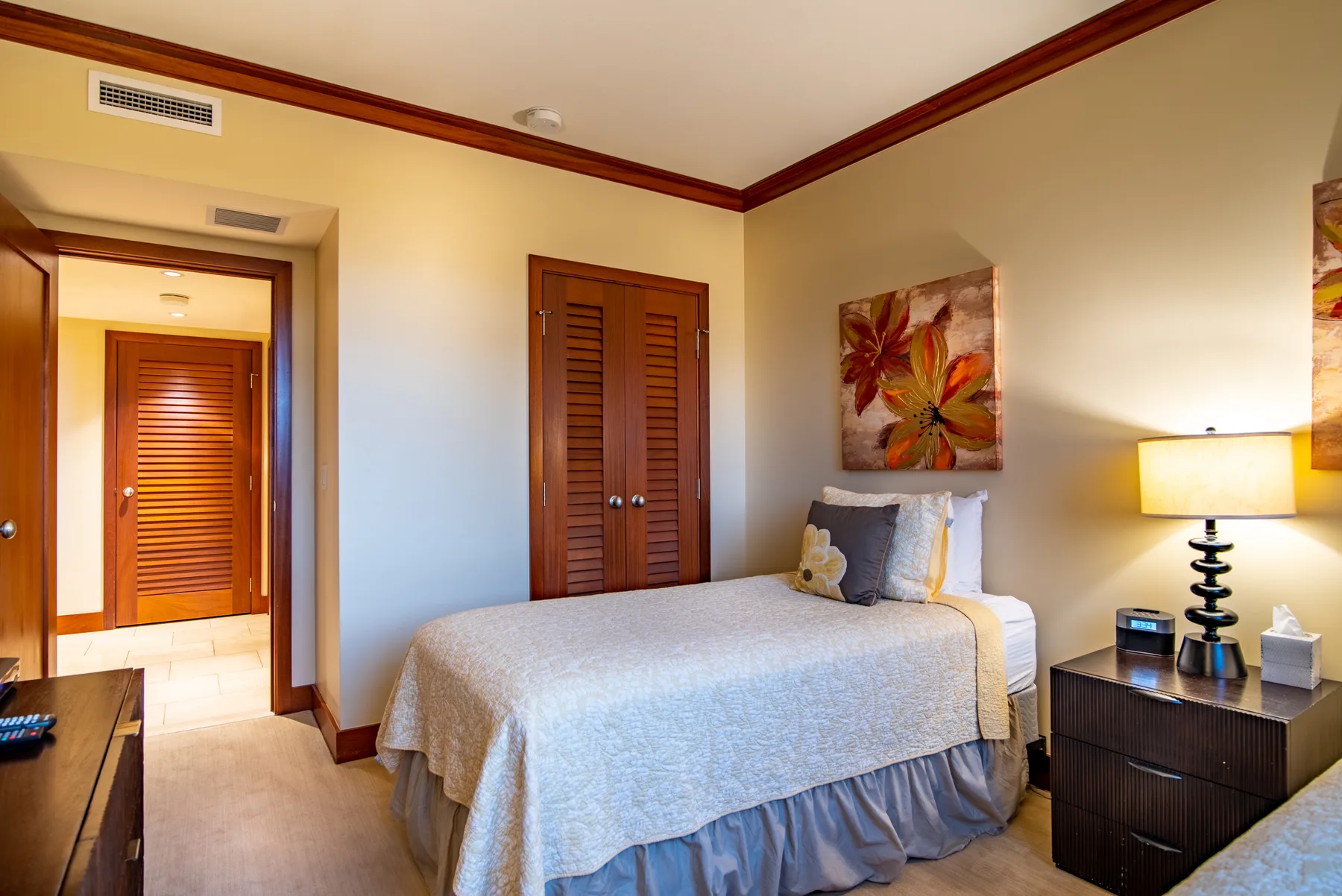 Un dormitorio con una cama tendida, contraventanas de madera y arte colorido en la pared.