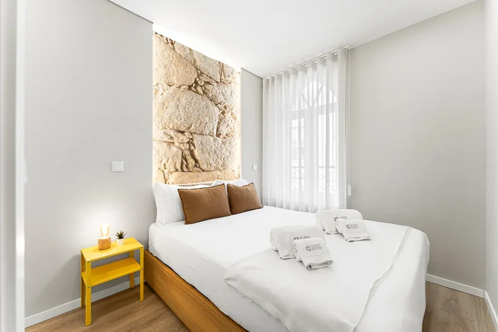 A bright bedroom with a white bed, brown pillows, and sheer curtains.