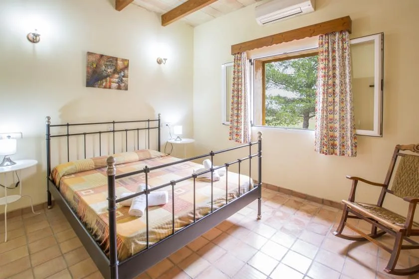 A bedroom with a metal bed, patterned bedding, and a window overlooking trees.