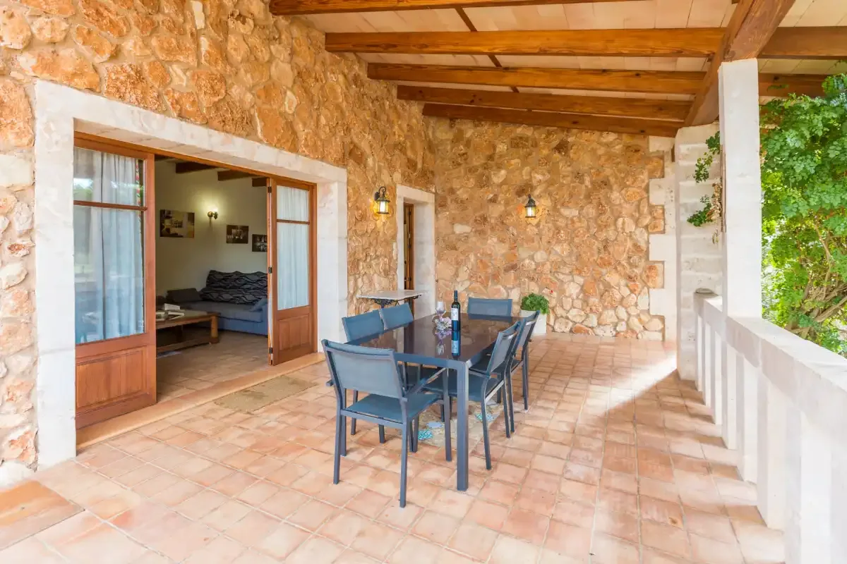 A covered stone patio with a dining table and an open doorway to a sitting area.