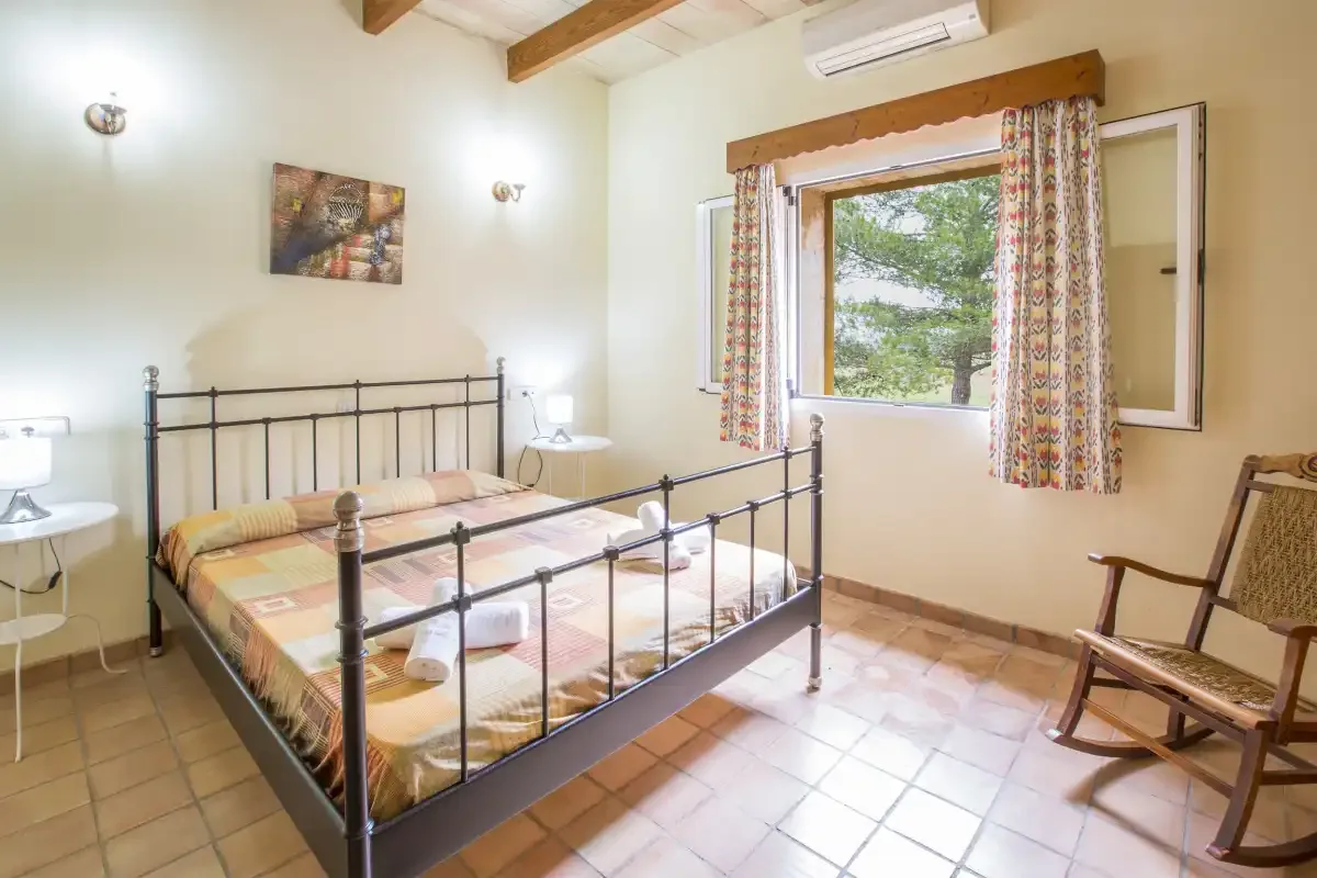 A bedroom with a metal bed, patterned curtains, and a window overlooking trees.