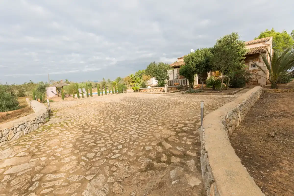 A stone-paved driveway curves toward a house surrounded by trees.