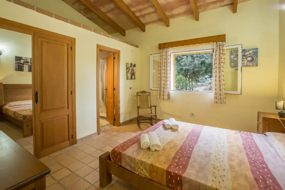 A bedroom with a bed, exposed wooden ceiling beams, and a window.