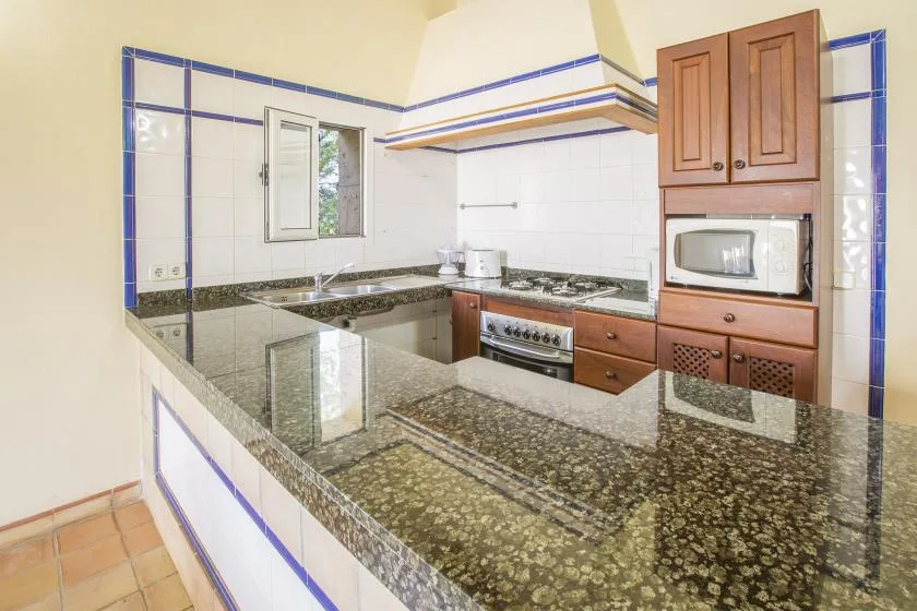 A tiled kitchen with dark countertops, a cooktop, and built-in appliances.