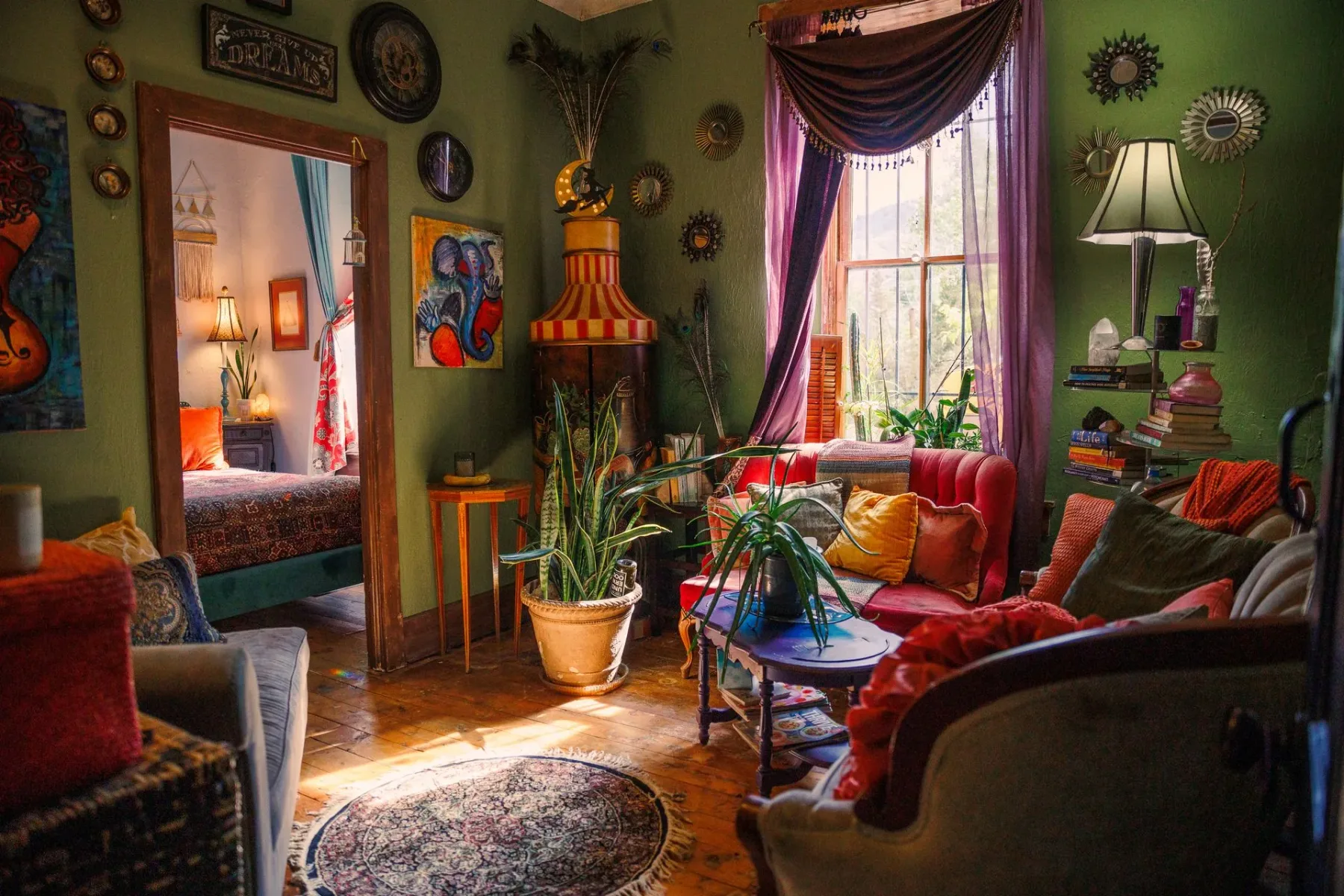 Sala de estar de estilo bohemio con paredes verdes, muebles coloridos, plantas y una ventana grande