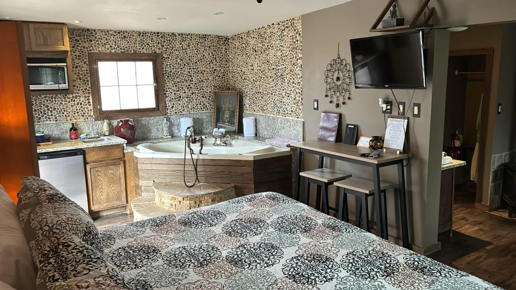 Habitación con bañera de hidromasaje, cocina pequeña, cama y televisor montado en la pared