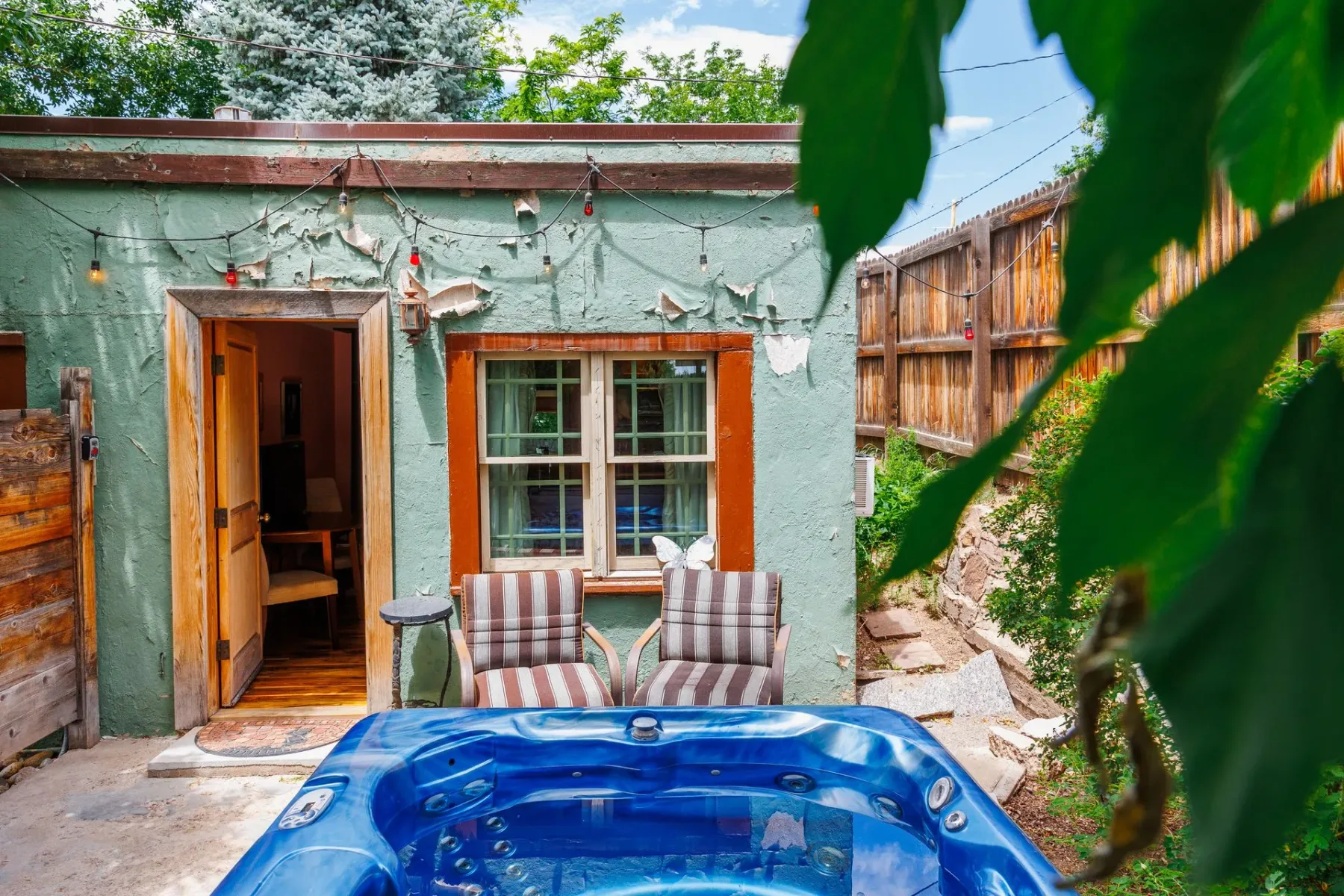 Jacuzzi azul en un patio de piedra junto a un edificio verde desgastado