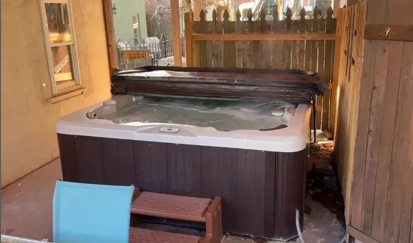 Jacuzzi con revestimiento de paneles oscuros en un porche con escalones y una silla cerca