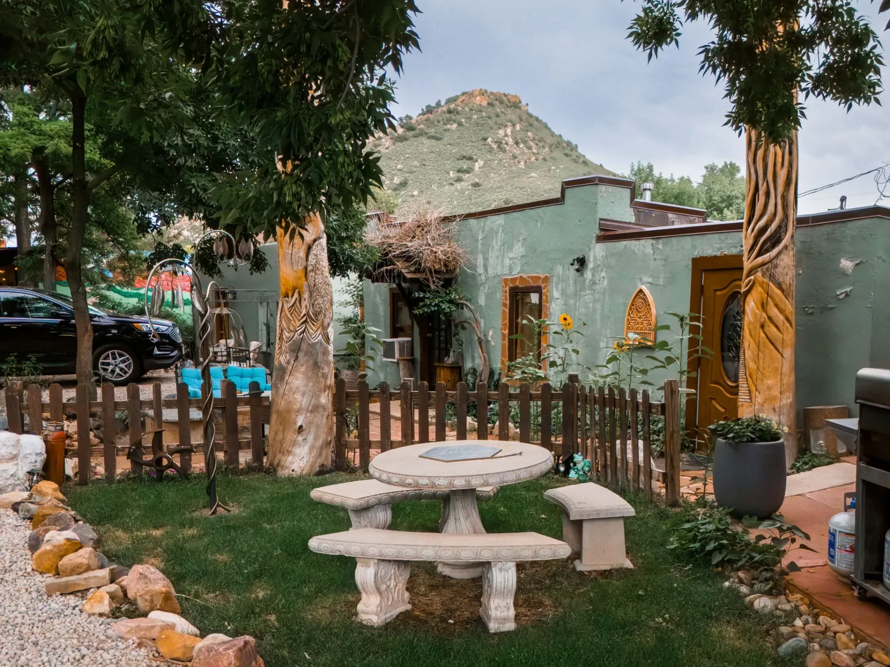 Zona de jardín con una mesa de piedra y bancos frente a un edificio con revestimiento de estuco verde