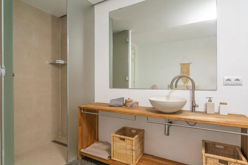 Un lavabo de baño con un espejo amplio, una pila y estantes abiertos.