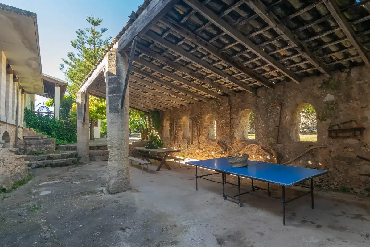 Un patio de piedra cubierto con una mesa de ping-pong azul y asientos de madera.