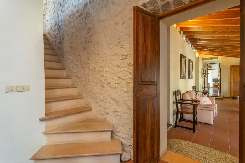 Un pasillo rústico interior con una escalera junto a una puerta de madera abierta.