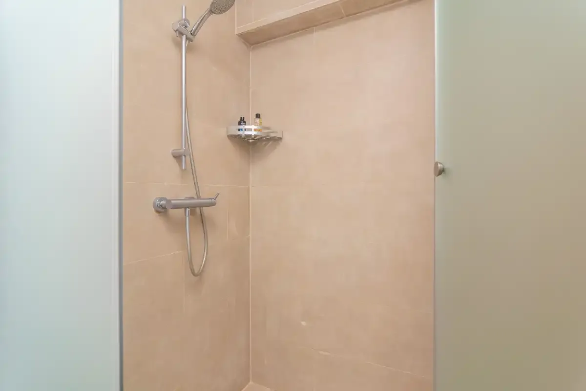 Una zona de ducha revestida de azulejos, con ducha de mano y controles en la pared.