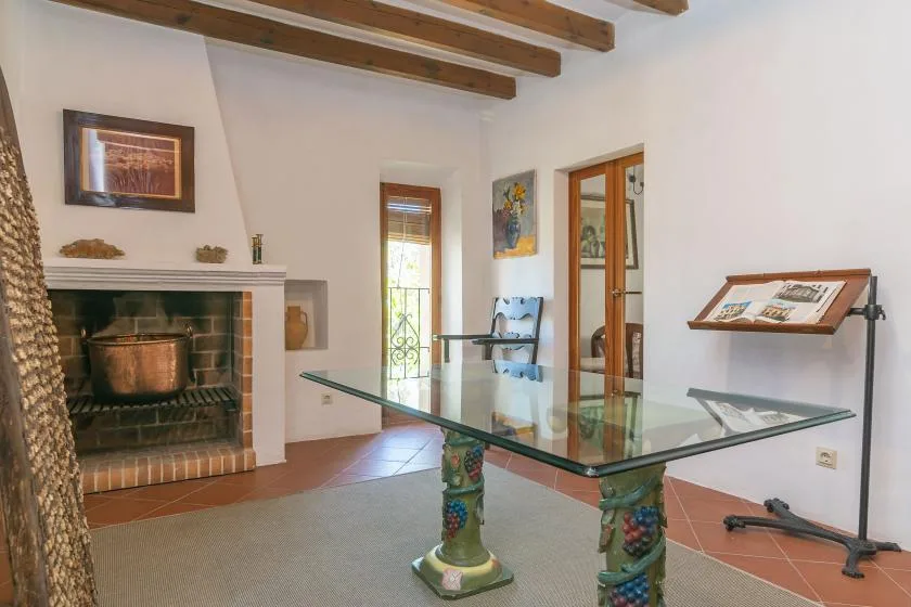 Comedor con una mesa de vidrio, una chimenea y vigas expuestas en el techo.
