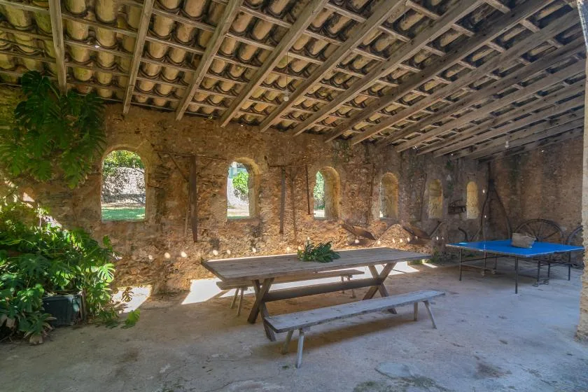 Una sala de piedra rústica con una larga mesa de picnic de madera bajo un techo de tejas expuesto.