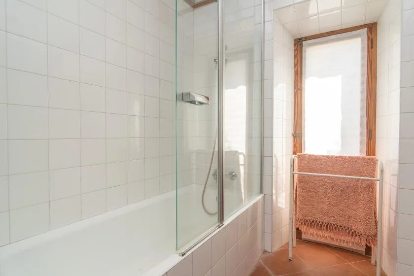 Un baño con azulejos, una ducha de vidrio y un toallero junto a la ventana.