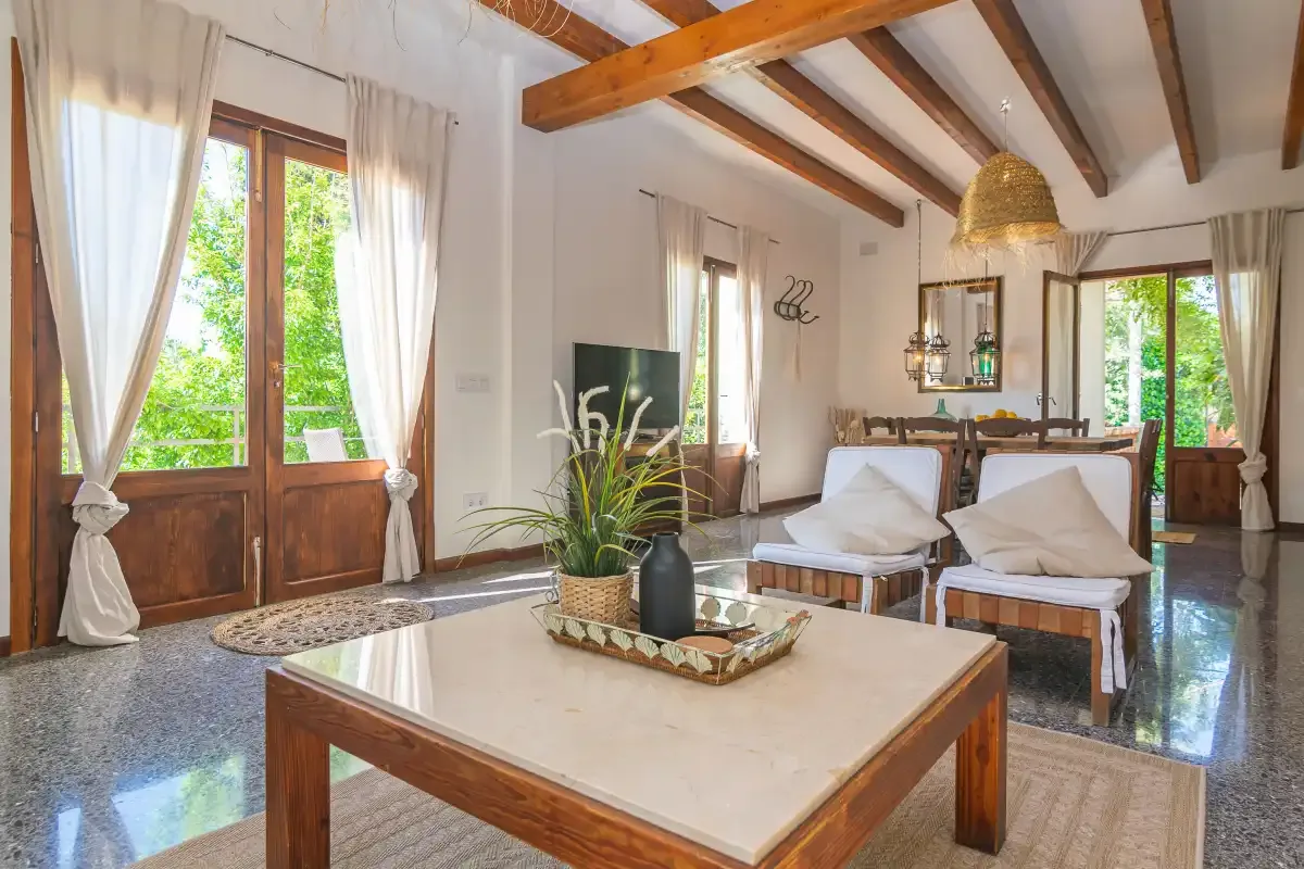 Una sala de estar luminosa con asientos, una mesa de centro y ventanas grandes.