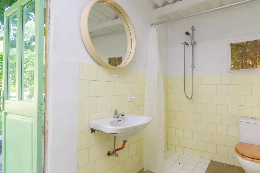 Un baño alicatado con lavabo de pared, espejo redondo y ducha.