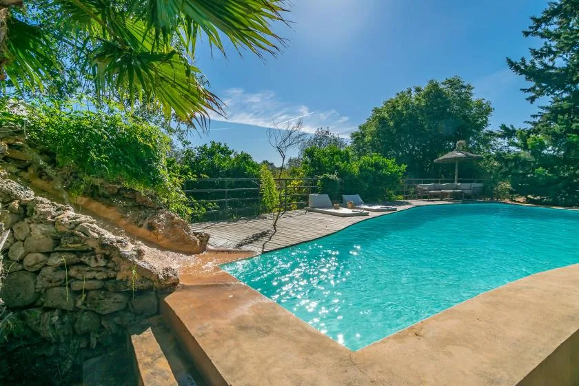 Una piscina turquesa está rodeada por una terraza de piedra y árboles frondosos.