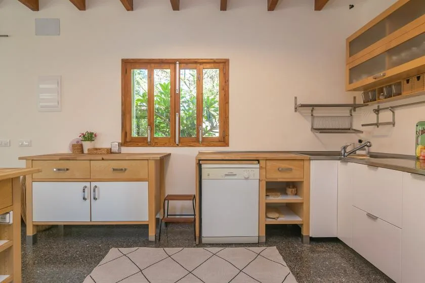 Una cocina con armarios de madera, un fregadero y una ventana con vistas a la vegetación.