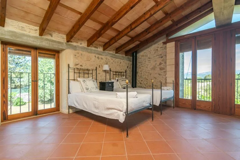 Un dormitorio con una cama de metal, paredes de piedra y grandes ventanas con marcos de madera.