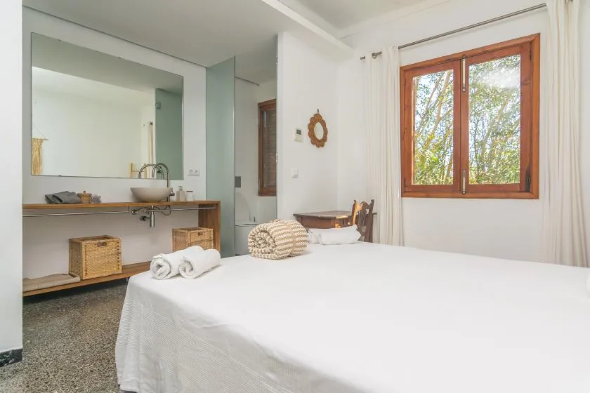 Un dormitorio con una cama blanca junto a una ventana con marco de madera.