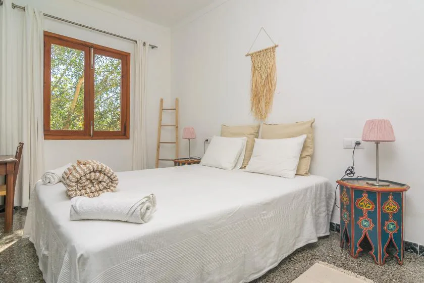 Un dormitorio luminoso con una cama bien tendida y una ventana con árboles frondosos.