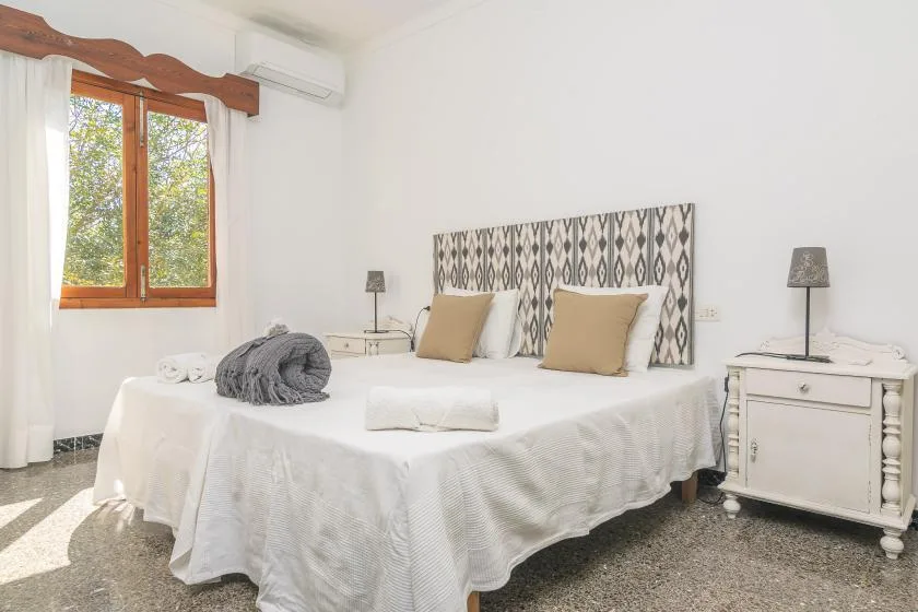 Un dormitorio luminoso con una cama doble, un cabecero estampado y una ventana.
