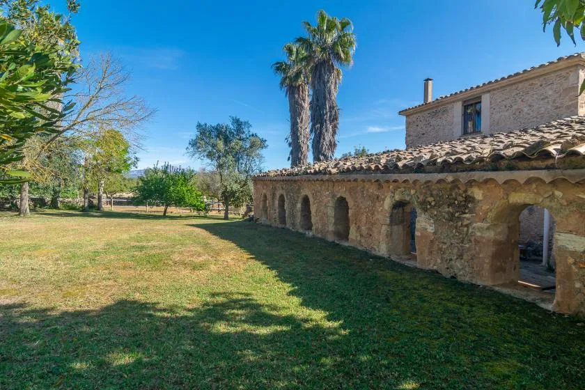 Un patio de césped junto a un edificio de piedra con una hilera de arcos.