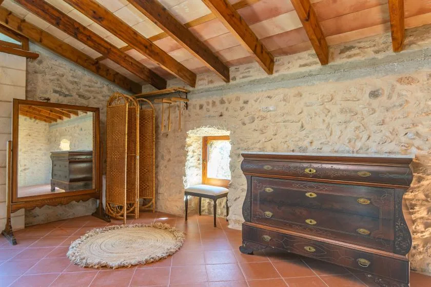 Un dormitorio rústico con una cómoda oscura, un biombo de mimbre y vigas expuestas en el techo.