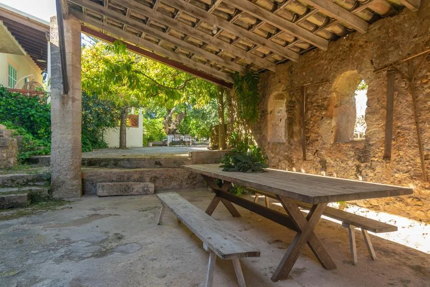 Un patio de piedra cubierto con mesas de madera y vegetación.