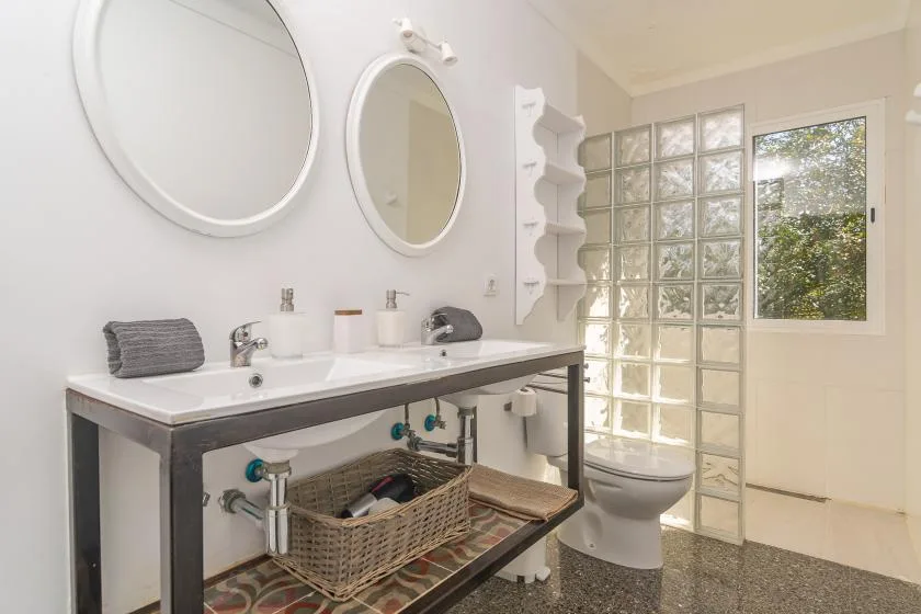 Un baño luminoso con lavabo doble, inodoro y pared de bloques de vidrio.