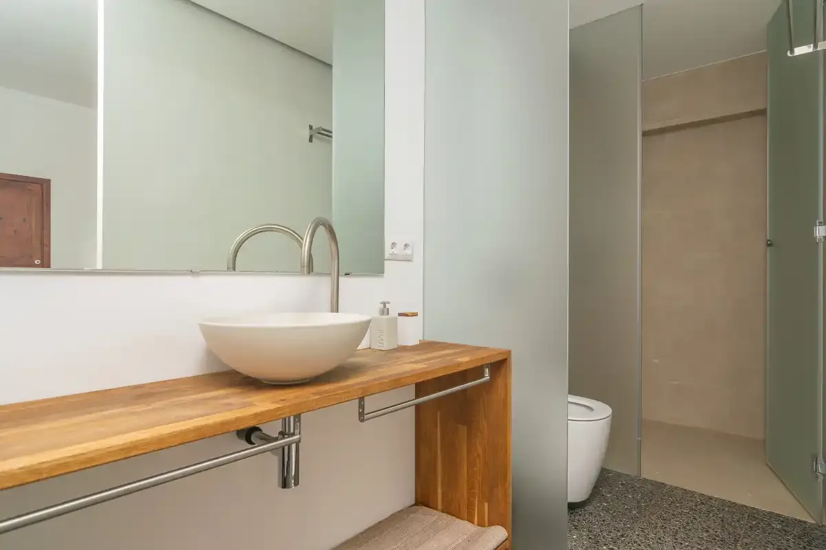 Un baño tiene un mueble de madera con lavabo sobre encimera junto a una ducha.