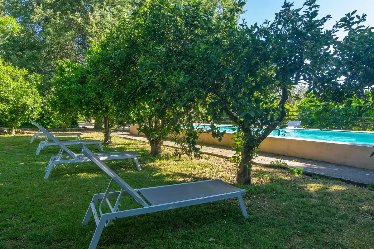 Una zona de descanso en el jardín junto a una piscina, a la sombra de los árboles.